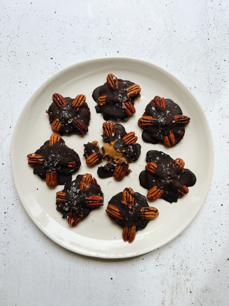 A white plate holds 8 candied dates topped with pecans and chocolate. 