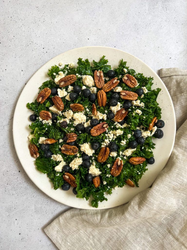 Plate with kale, pecans, goats cheese and blueberries, sitting on top of a cloth napkin.