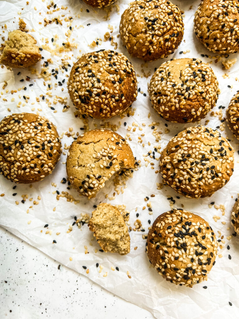 Sesame covered cookies on a tray surrounded by crumbs