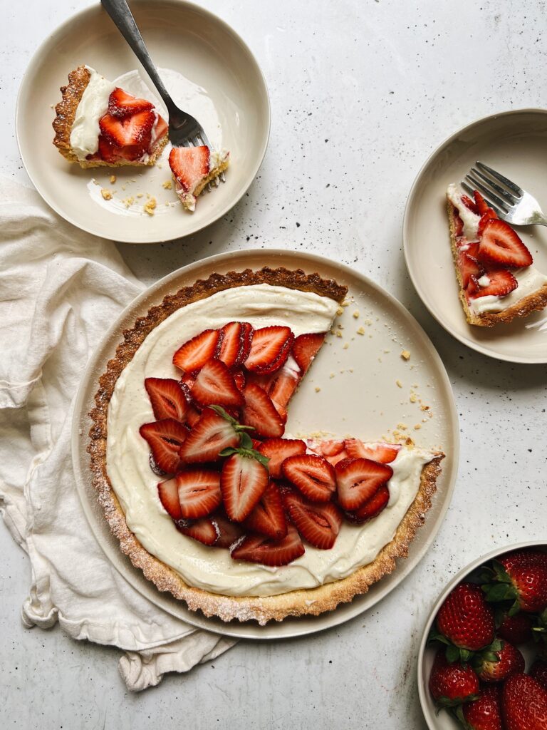 Strawberry tart with a slice removed. A bowl of strawberries sits alongside. 