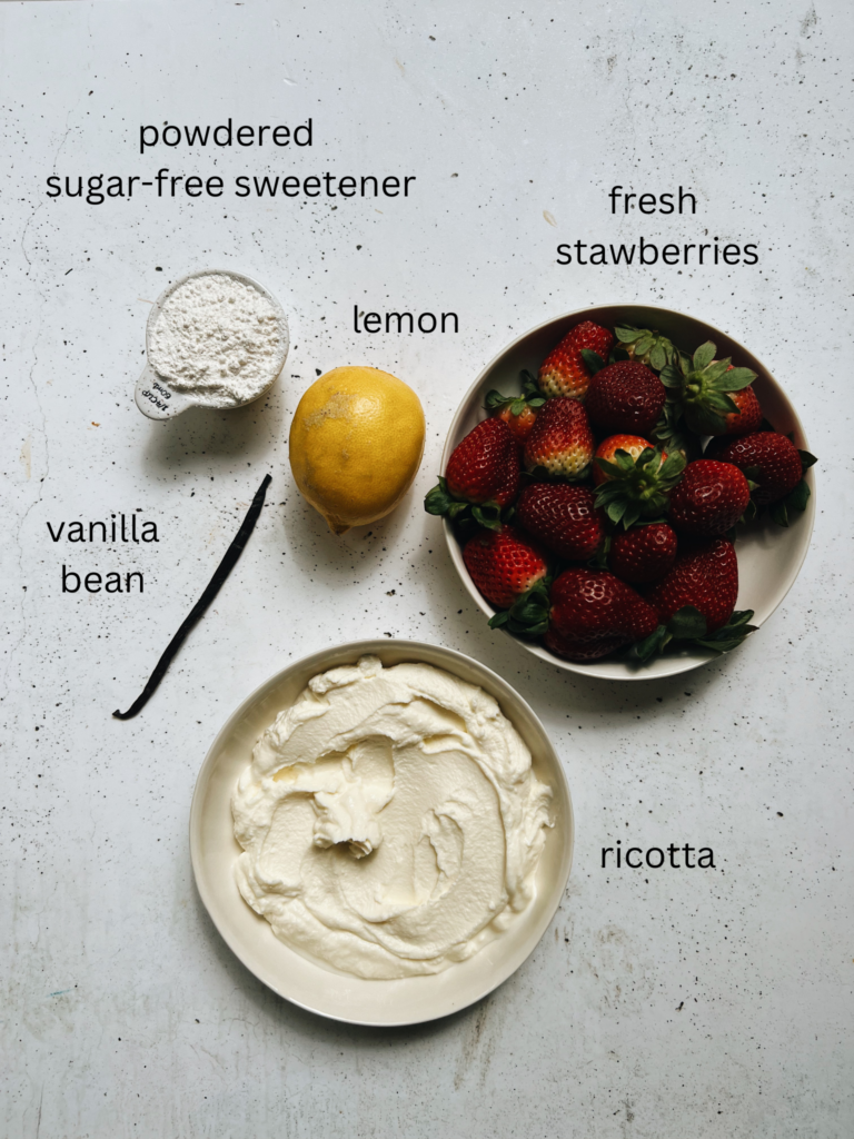 A vanilla bean, a lemon, a bowl of strawberries, a measuring cup of powdered sweetener and a bowl of ricotta sit on a bench.
