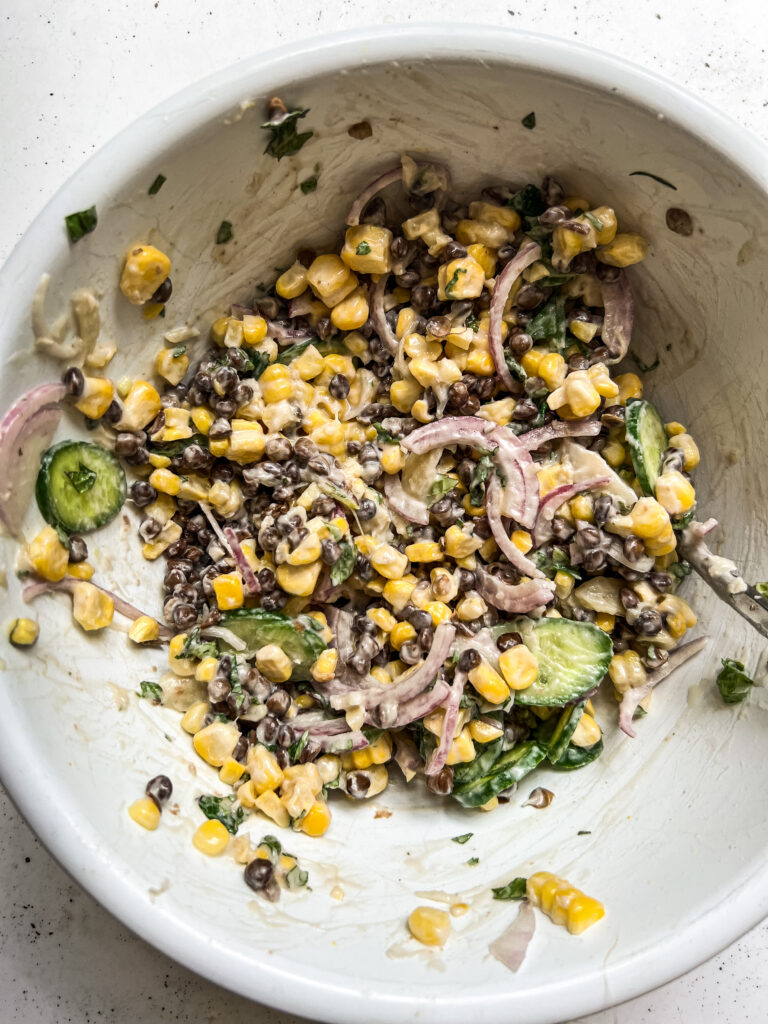 A bowl with a mix of corn, lentils, cucumber, red onion