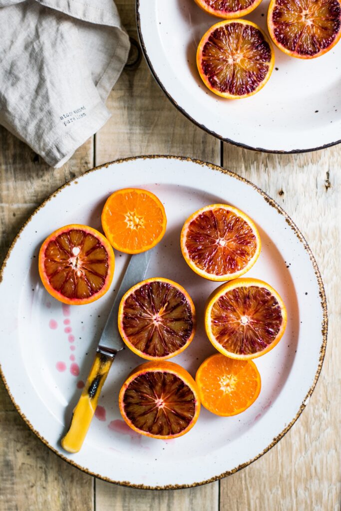 A cloth napkin sits beside a plate of blood oranges cut in half with a knife 